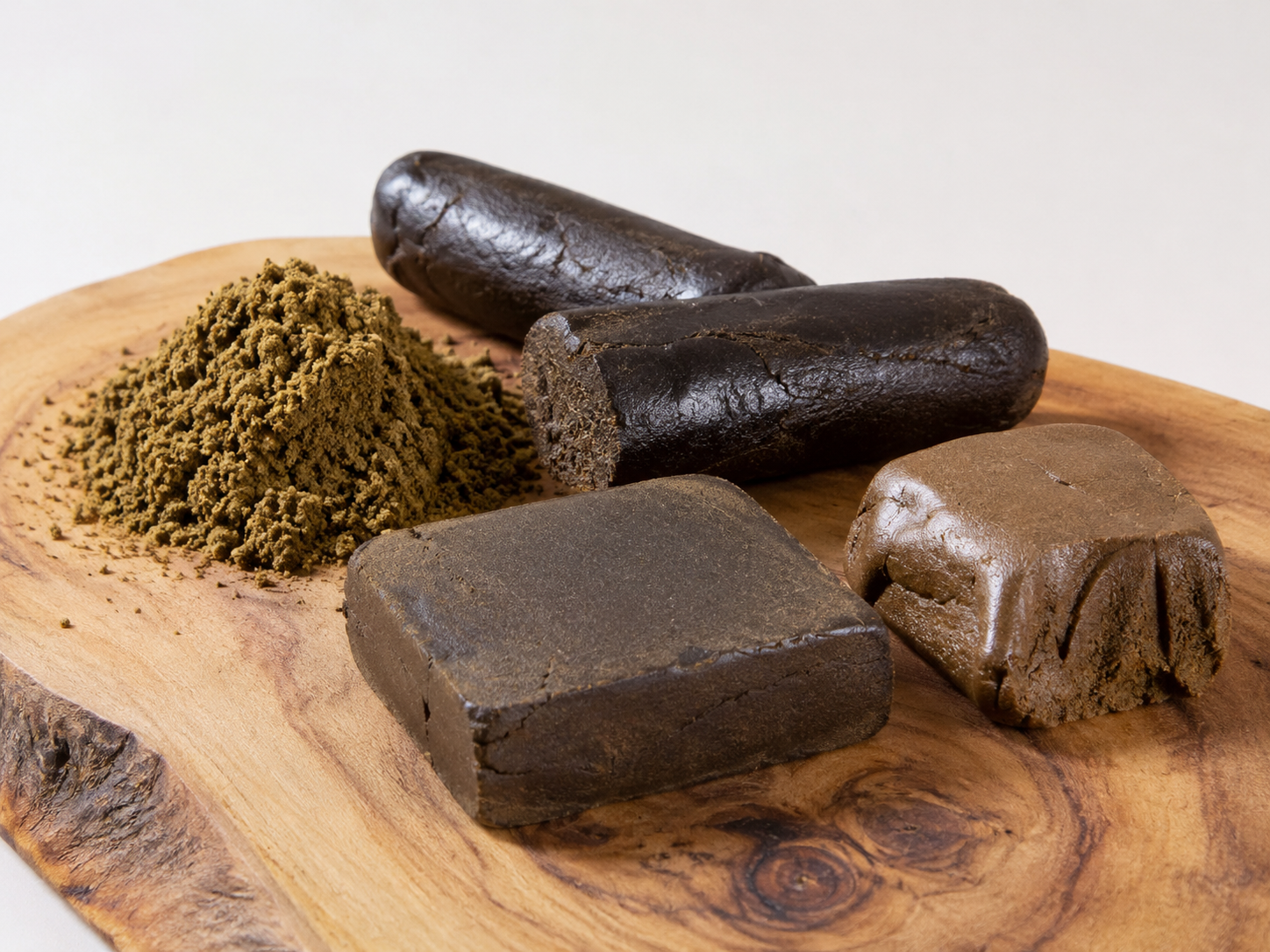 Various forms of sifted and pressed CBD hash in Switzerland, with dry, soft, and creamy textures, displayed on a wooden base.